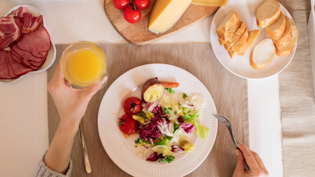 A top-view of a delicious breakfast setting featuring a salad, bread, cheese, tomatoes, and orange juice.